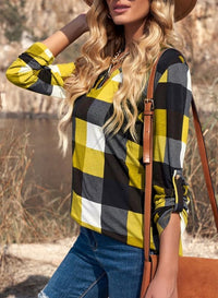 Frau in kariertem Hemd, gelb-schwarz, mit brauner Tasche, Outdoor-Hintergrund.