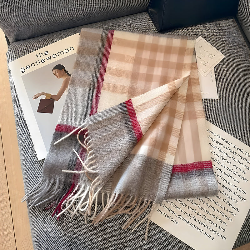 Beigefarbener Karoschal aus Wolle mit Fransen, auf grauem Sofa liegend, neben Zeitschriften.