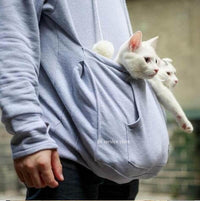 Person in grauem Hoodie mit zwei weißen Katzen in der Bauchtasche, gemütlich, ideal für Katzenliebhaber.