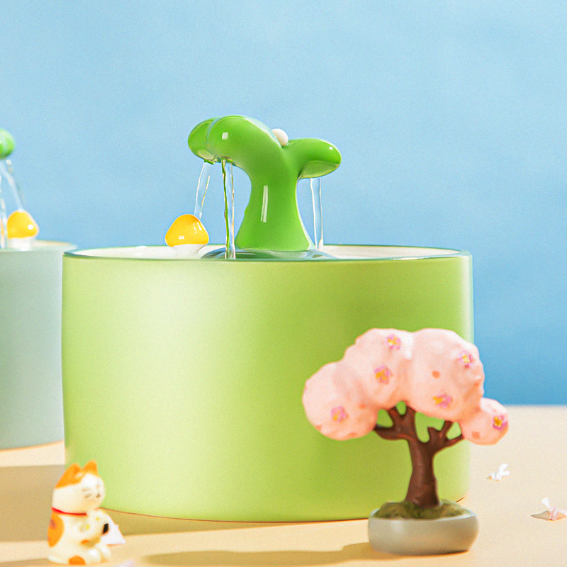 Grüner Katzenbrunnen mit Wasserstrahl, Keramik, dekorativer Baum, Spielzeugkatze, blauem Hintergrund.