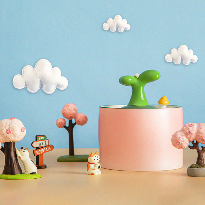 Rosa Luftbefeuchter mit grünem Sprühkopf, dekoriert mit Miniaturbäumen und Wolken.