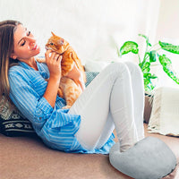 Frau mit Katze und grauem Fußwärmer auf Sofa, gemütlich, entspannend, Wohnzimmer.