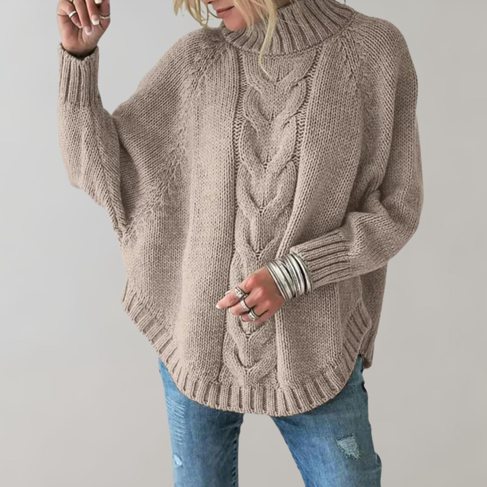 Frau trägt khakifarbenen Strickpullover mit Zopfmuster, Rollkragen und blauen Jeans.
