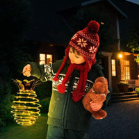 Kind mit roter Mütze hält leuchtende Laterne und Teddybär, draußen bei Nacht.