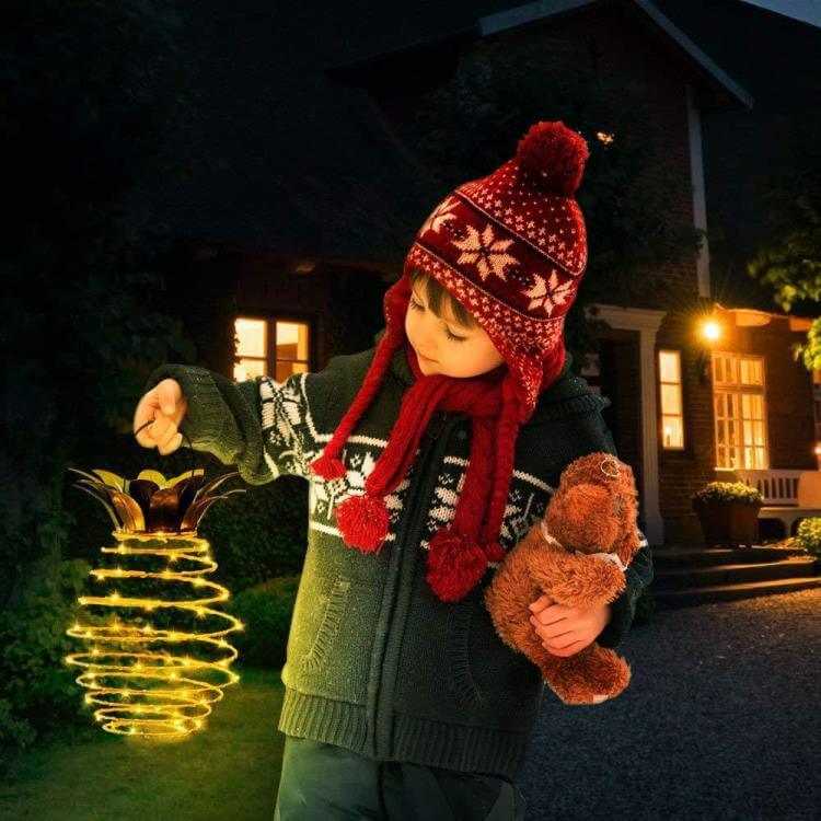 Kind mit roter Mütze hält leuchtende Laterne und Teddybär, draußen bei Nacht.