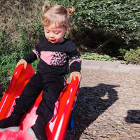 Kleinkind in schwarzem Outfit mit Leopardenmuster rutscht auf roter Rutsche im Freien.