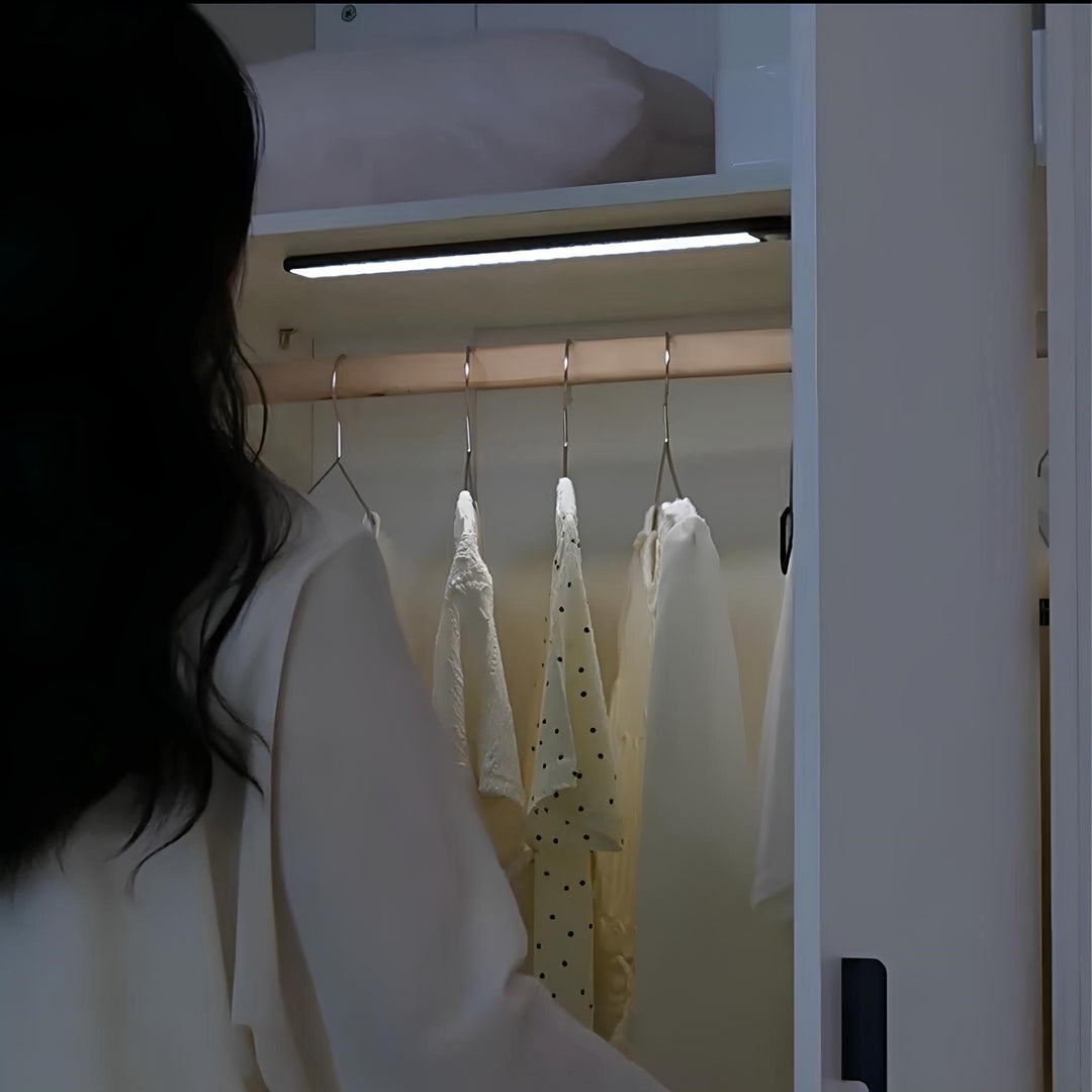 Frau öffnet Kleiderschrank mit beleuchteter Kleiderstange, weiße Blusen, modernes Design.