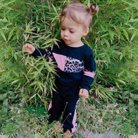 Kleinkind in schwarzem und rosa Leopardenmuster-Trainingsanzug im Garten.