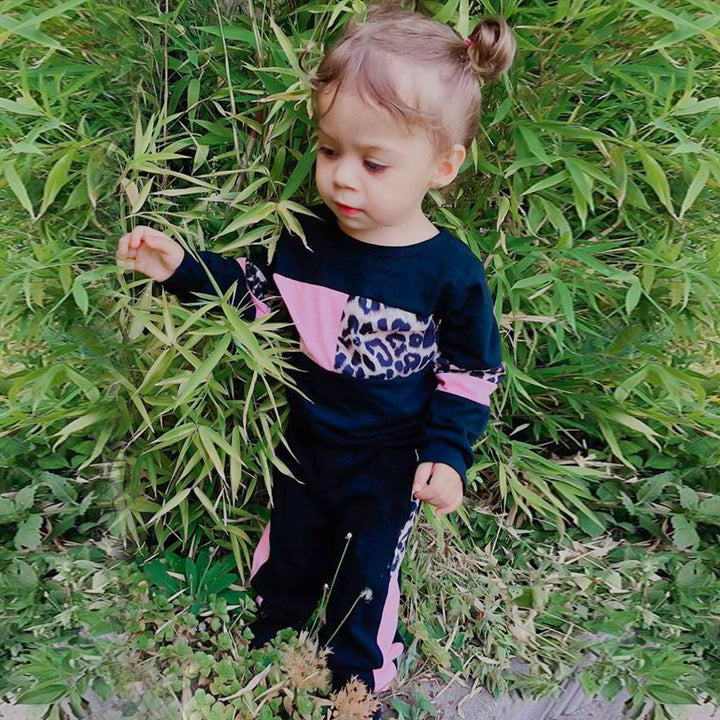 Kleinkind in schwarzem und rosa Leopardenmuster-Trainingsanzug im Garten.