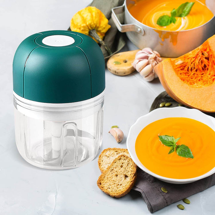 Grüner Knoblauchpresse Zerkleinerer, Kunststoff, neben Kürbissuppe und Brot auf Küchentisch.