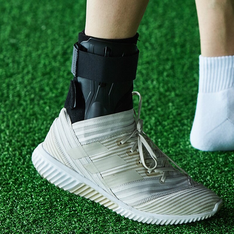 Weiße Sportschuhe mit Knöchelbandage auf grünem Kunstrasen.