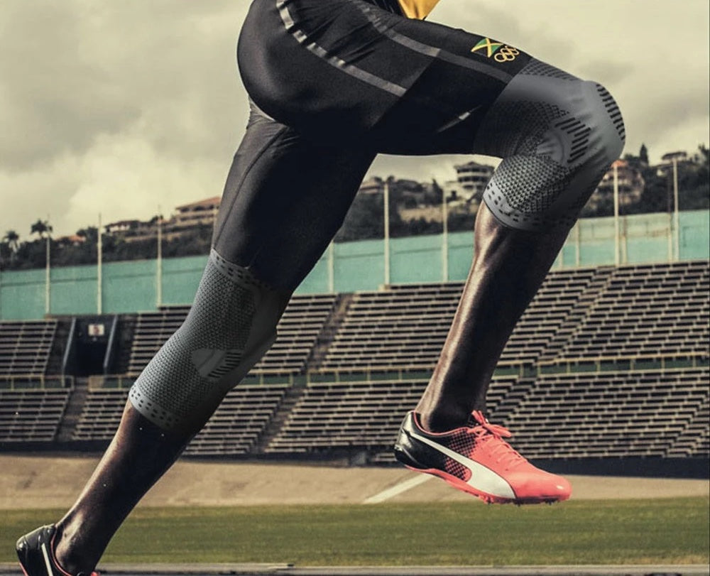 Läufer in schwarzen Kompressionshosen und pinken Sportschuhen auf Stadionbahn.