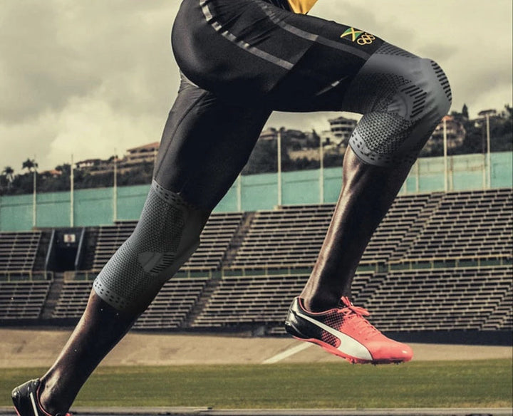 Läufer in schwarzen Kompressionshosen und pinken Sportschuhen auf Stadionbahn.