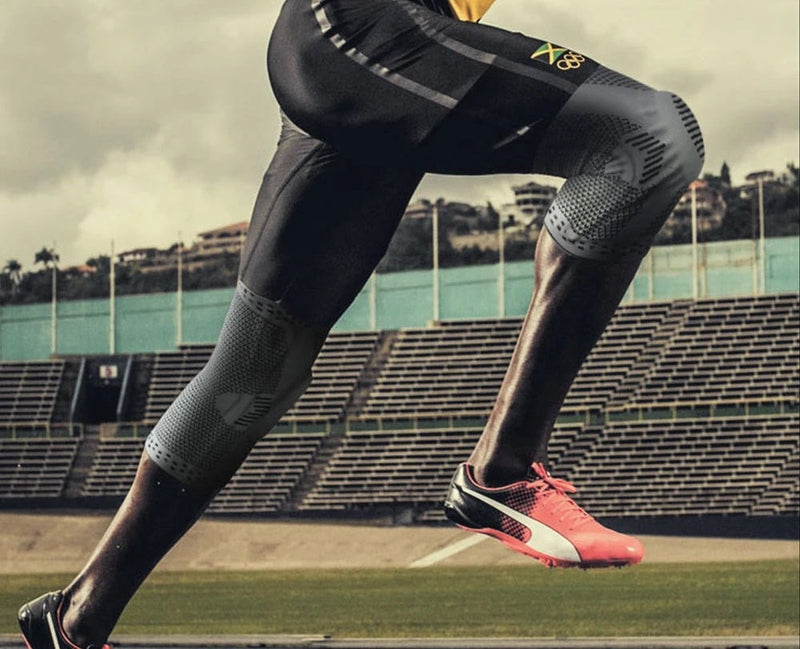 Läufer in schwarzen Kompressionshosen und pinken Sportschuhen auf Stadionbahn.