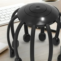Schwarzer Kopfmassagegerät mit acht Beinen auf Schreibtisch, neben Tastatur und Kaffeetasse.