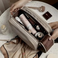 Kosmetiktasche beige, gefüllt mit Make-up-Produkten, auf Tisch mit Seidentuch und Pinsel.