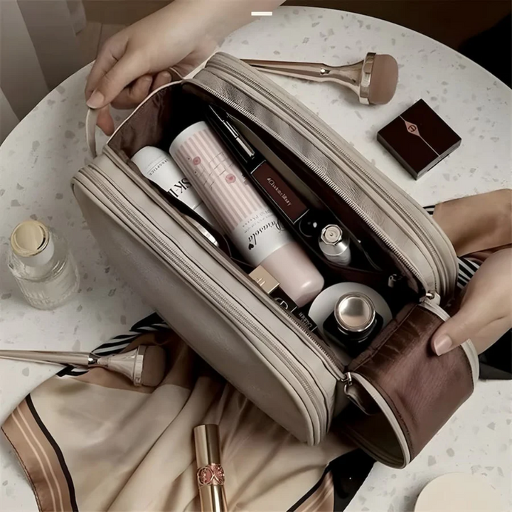 Kosmetiktasche beige, gefüllt mit Make-up-Produkten, auf Tisch mit Seidentuch und Pinsel.