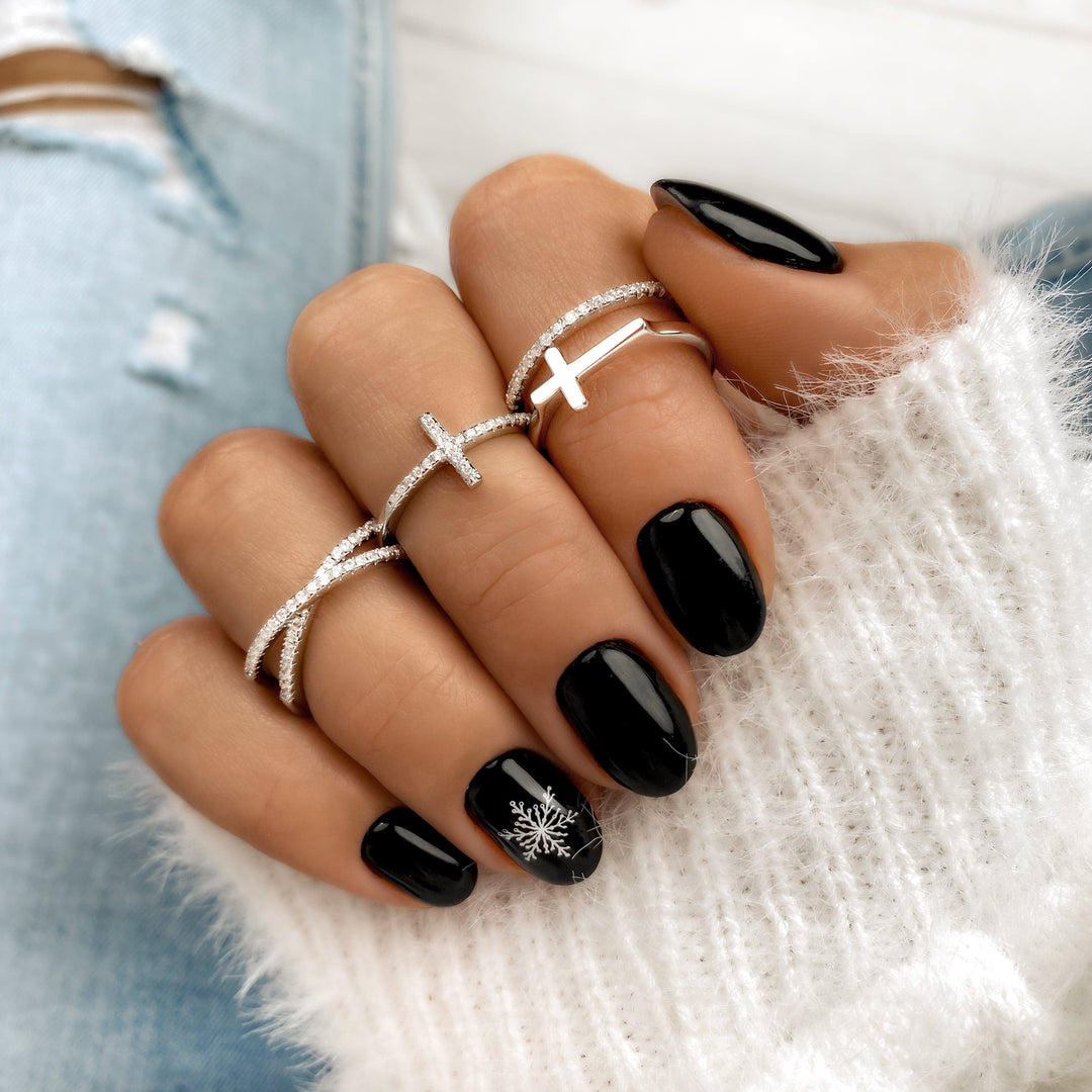 Silberne Kreuzringe an Hand mit schwarzem Nagellack und weißem Pullover.