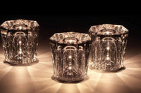 Drei leuchtende Kristall-Teelichthalter, facettiert, elegant, stimmungsvoll, auf dunklem Hintergrund.