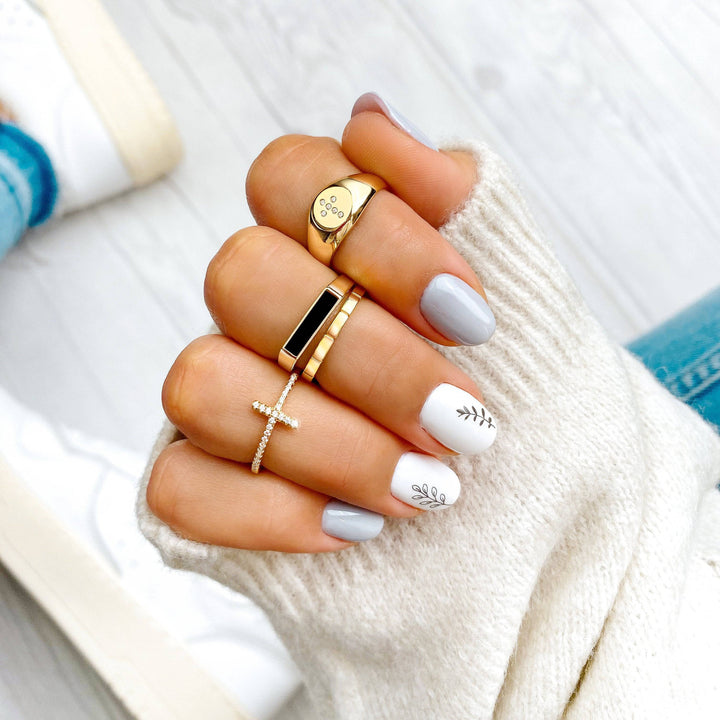 Frau mit vier Ringen: Gold, Kreuz, Schwarz, Herz. Weiße Nägel mit Blattdesign.