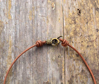 Braunes Lederhalsband mit Messingverschluss auf rustikalem Holzhintergrund.