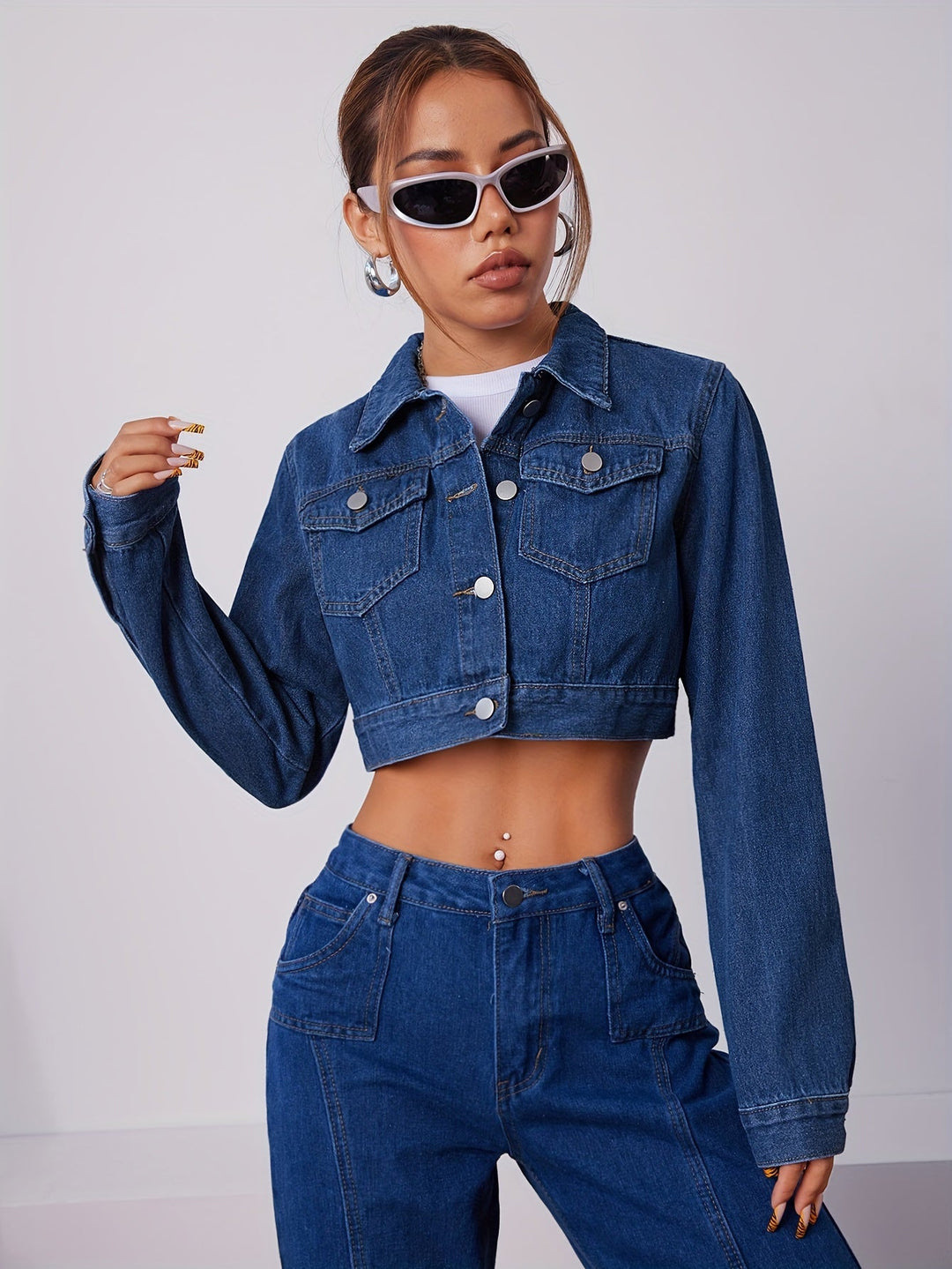 Frau in blauer Jeansjacke und Jeans, trägt weiße Sonnenbrille, modisches Outfit.