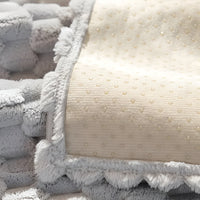 Weiche graue und cremefarbene Decke mit Fransen, gepunktetes Muster, kuscheliges Wohnaccessoire.