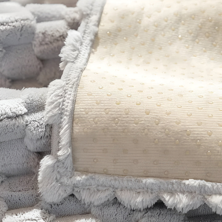 Weiche graue und cremefarbene Decke mit Fransen, gepunktetes Muster, kuscheliges Wohnaccessoire.