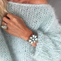 Frau mit hellblauem Strickpullover, türkisfarbenem Armband und Ring mit großem Stein.