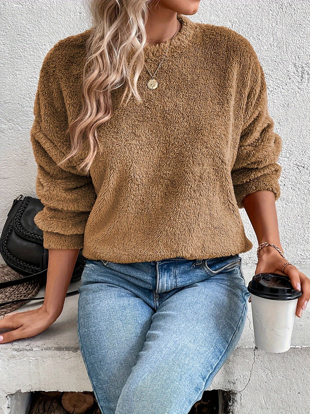 Frau in braunem Fleece-Pullover, blaue Jeans, hält Kaffeebecher, modisch, lässig, Herbstoutfit.