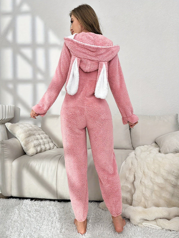 Frau in rosa Plüsch-Pyjama mit Kapuze und Hasenohren, gemütliche Loungewear, Wohnzimmer.
