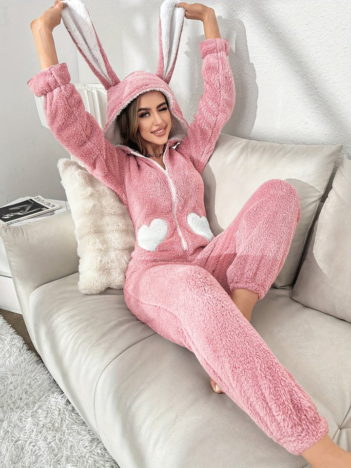 Frau in rosa Hasen-Overall aus Fleece auf Sofa, gemütliche Loungewear, Kapuze mit Ohren.