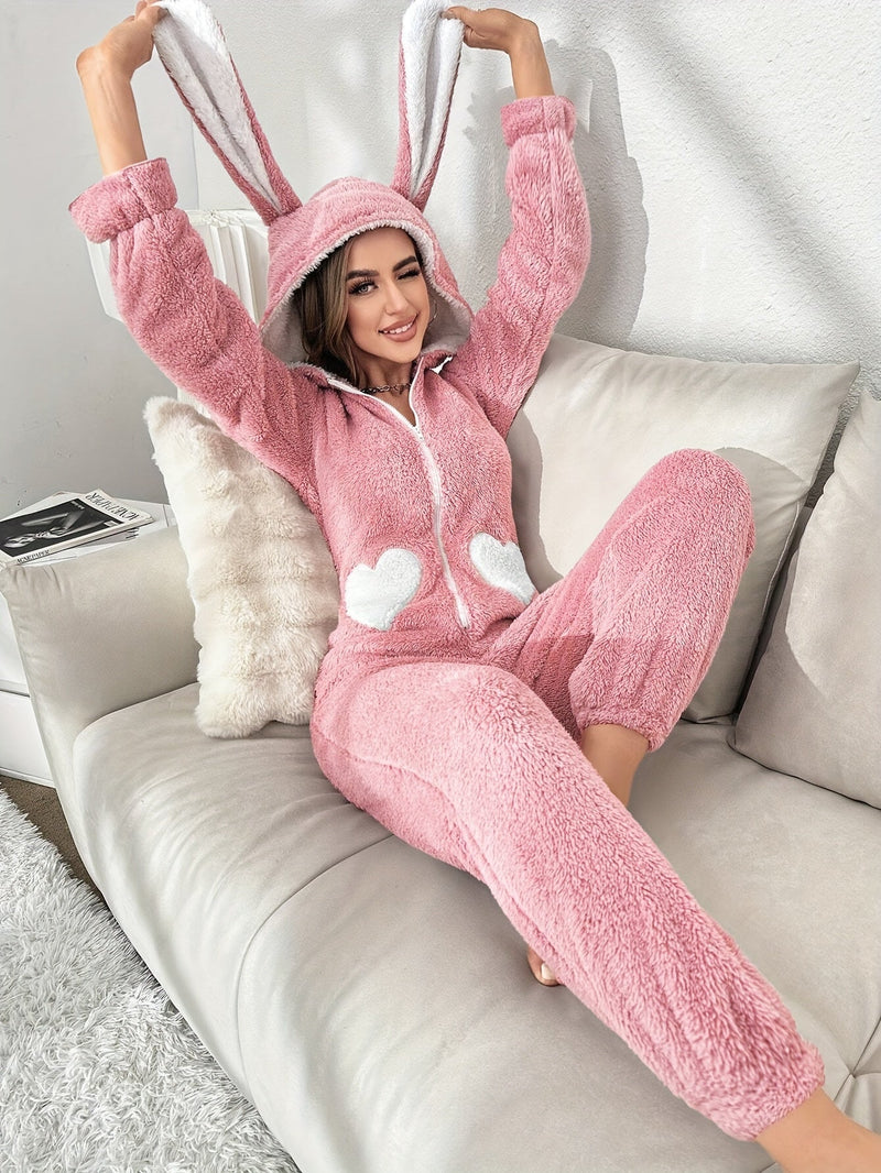 Frau in rosa Hasen-Overall aus Fleece auf Sofa, gemütliche Loungewear, Kapuze mit Ohren.