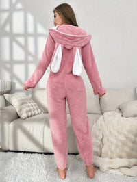 Frau im rosa Plüsch-Einteiler mit Kapuze und Hasenohren, gemütliche Loungewear.