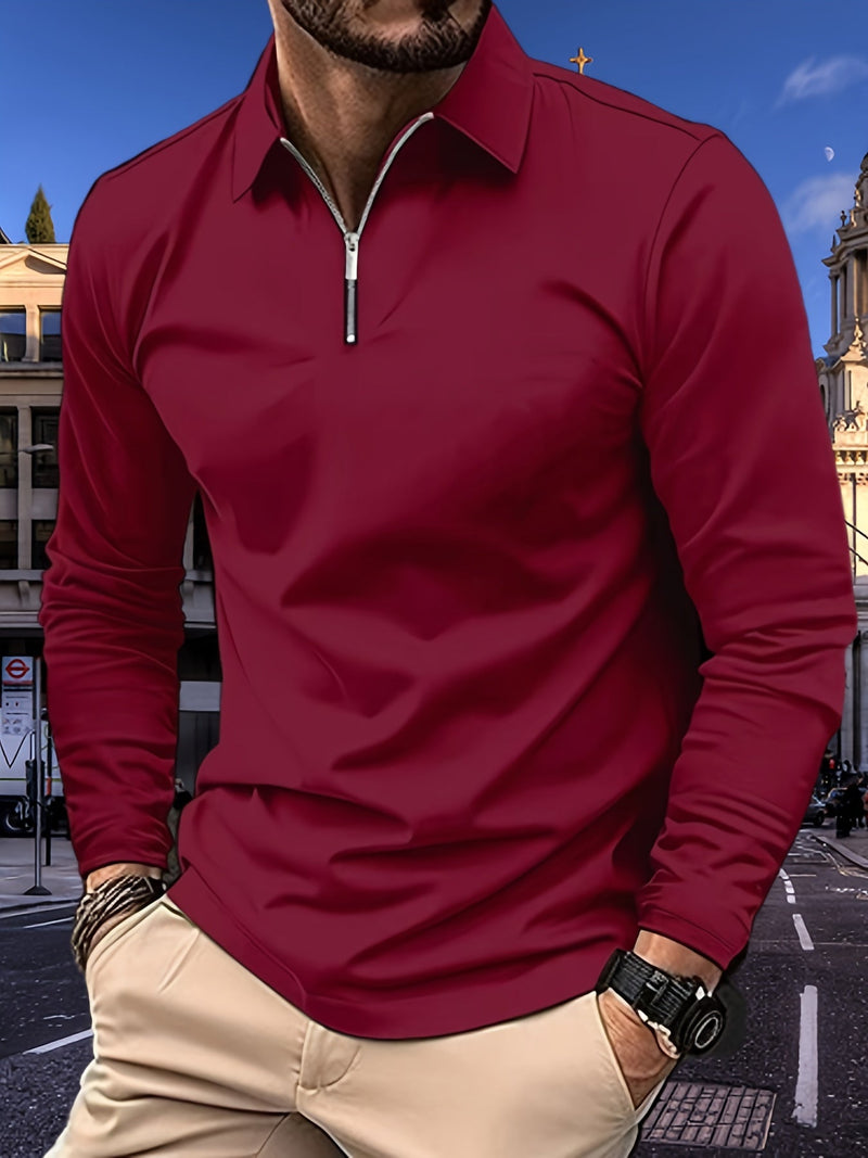 Mann in rotem Langarmshirt mit Reißverschluss, beige Hose, Stadt im Hintergrund.