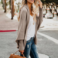 Frau in beiger Strickjacke, weißem T-Shirt und Jeans auf Straße, modische Herbstkleidung.