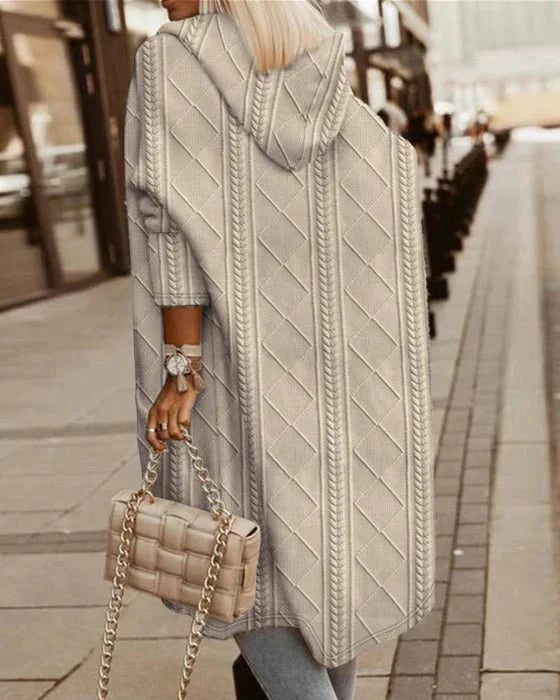 Frau in langem, grauem Strick-Cardigan mit Kapuze, hält beige gesteppte Handtasche.