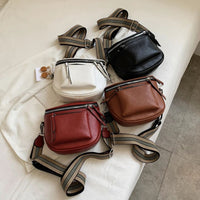 Vier Leder-Umhängetaschen in Schwarz, Weiß, Braun und Rot auf einem Bett.