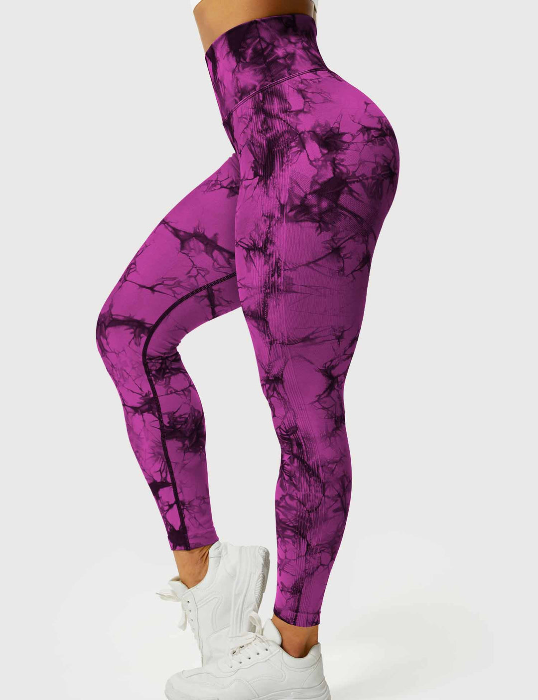 Frau in lila-pinken Batik-Leggings, hohe Taille, sportlich, mit weißen Turnschuhen.