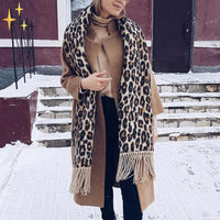 Frau mit Leopardenmuster-Schal und braunem Mantel im Schnee, Wintermode-Trend.