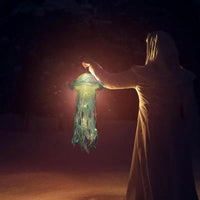 Person in Umhang hält leuchtende Laterne in der Dunkelheit, mystische Atmosphäre, Nacht.