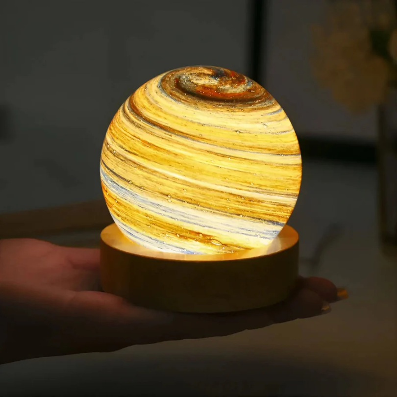 Leuchtende Saturn-Lampe auf Holzsockel, dekorative LED-Nachtlampe, gelb-orange, Hand gehalten.