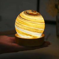 Leuchtende Saturn-Lampe auf Holzsockel, dekorative LED-Nachtlampe, gelb-orange, Hand gehalten.