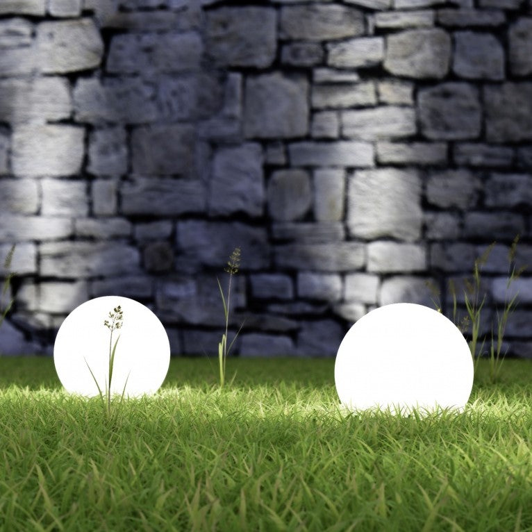 Zwei leuchtende LED-Kugellampen im Garten vor einer Steinmauer bei Nacht.