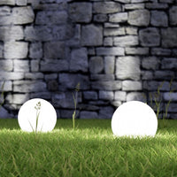 Zwei leuchtende LED-Kugellampen im Garten vor einer Steinmauer bei Nacht.