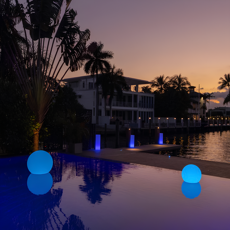 Leuchtende blaue Kugeln am Pool bei Sonnenuntergang, moderne Villa im Hintergrund.