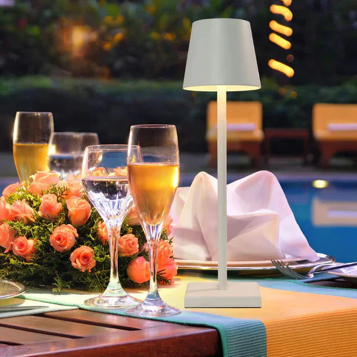 Tischlampe am Pool, umgeben von Sektgläsern und Blumen, ideal für elegante Abendessen.