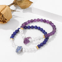 Zwei Armbänder aus Amethyst und Lapislazuli mit Perlen auf weißem Hintergrund.