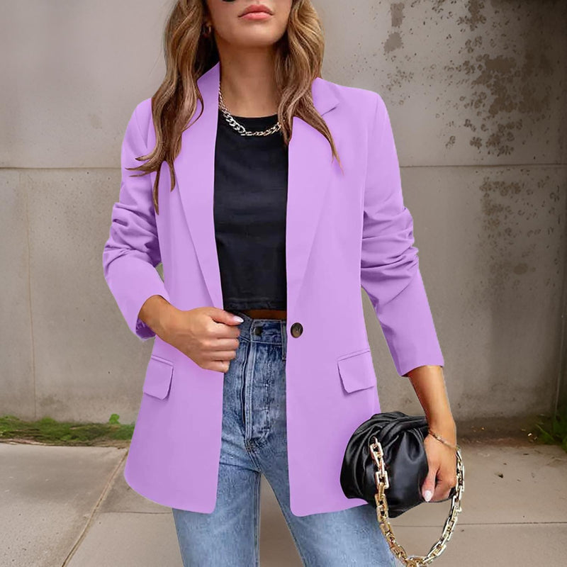 Frau in lila Blazer, schwarzem Top, Jeans, hält schwarze Tasche mit Kette, modisch, urban.