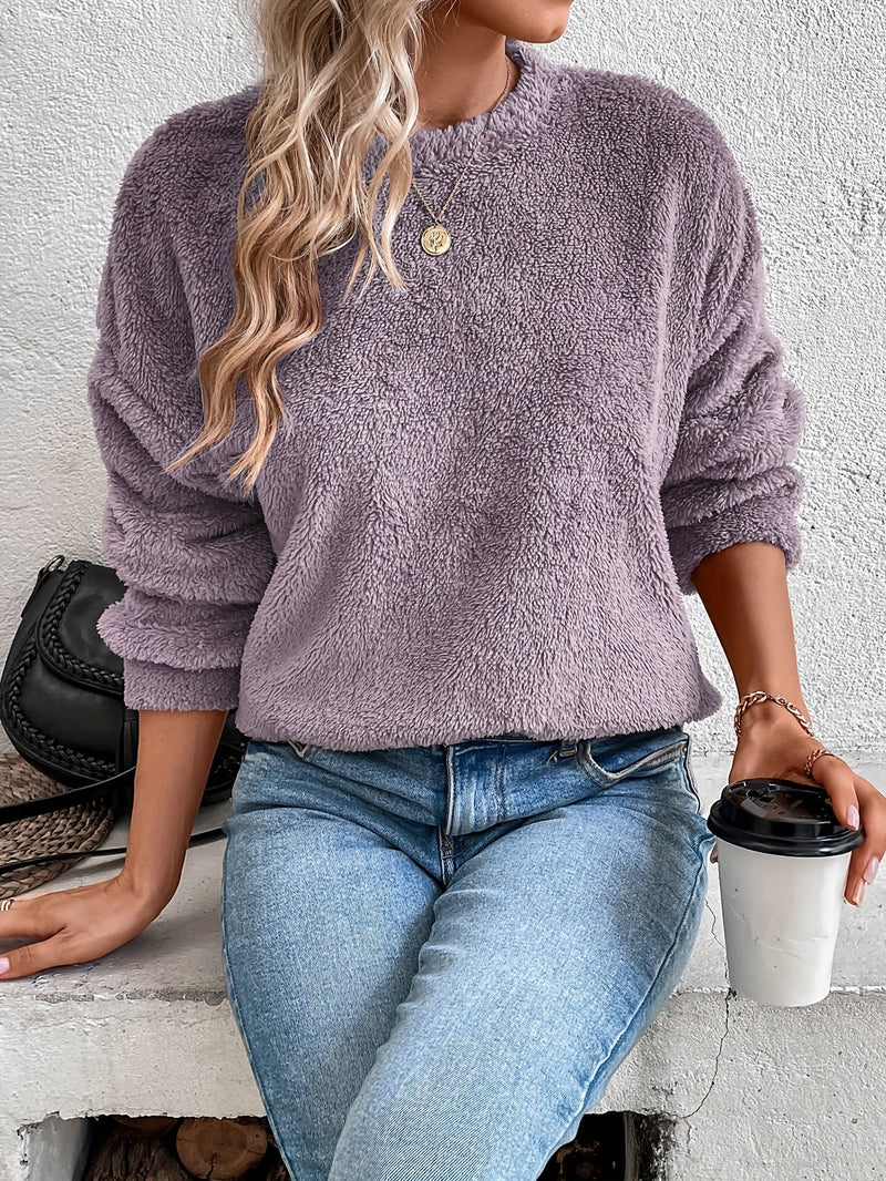 Frau in lila Fleece-Pullover, blaue Jeans, hält Kaffeebecher, modisch, lässiger Look.